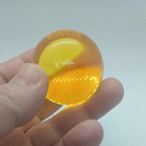 May include: A clear, spherical object with a yellow and orange color scheme. The object is held in a hand against a white background. The sphere appears to be made of a translucent material.