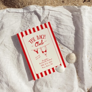May include: A red and white striped invitation card for "The Bach Club" bachelorette weekend, with bikini illustrations, resting on a white cloth and sand. The card includes the text "Suns out, buns out!" and event details.