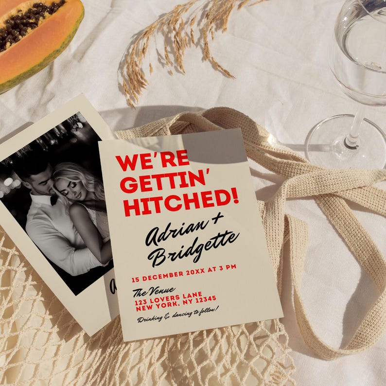 May include: A tan wedding invitation with red text that reads "We're Gettin' Hitched!" with the names Adrian and Bridgette. The date and time of the wedding is December 15th at 3 PM. The venue is 123 Lovers Lane, New York, NY 12345. The invitation says "Drinking & dancing to follow!"