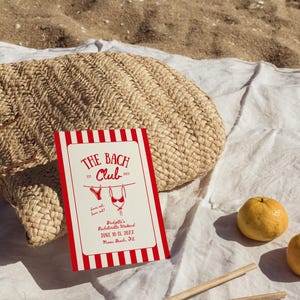 May include: A beach-themed invitation card with red and white stripes, featuring the text "THE BACH CLUB" and a bikini illustration. The card is on a white cloth next to a woven straw bag and two oranges.