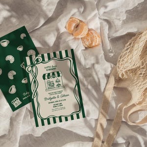 May include: An overhead shot features a green and white invitation with the text "A little bean is brewing" and a matching green card with coffee and croissant illustrations. A string bag and mandarin orange slices are also present.