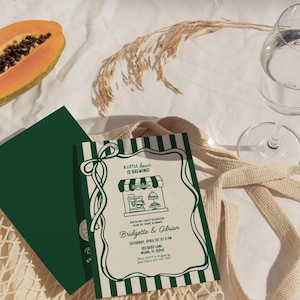 May include: A baby shower invitation with a green and white striped border and the text "A Little Bean is Brewing!". The invitation includes the names Bridgette & Adrian, date, time, and address. A slice of papaya and a glass of water are also visible.