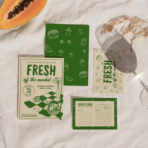 Op de afbeelding: Een verzameling groene en cr&egrave;mekleurige briefpapier met de tekst "FRESH off the market". Het briefpapier omvat uitnodigingskaarten, receptkaarten en decoratieve kaarten met illustraties van fruit en groenten. Een halve papaja is zichtbaar.