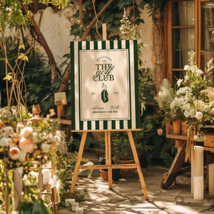 May include: A wooden easel displays a sign with green and white stripes. The sign reads "Welcome to The Golf Club" with a golf bag illustration and "Adrian's 30th Birthday Par-Tee". The scene is outdoors with floral arrangements.