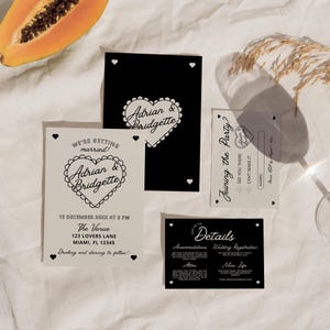 Op de afbeelding: Zwart-witte huwelijksuitnodigingsset met een hartvormig ontwerp met de namen Adrian en Bridgette. De uitnodiging bevat details over de datum, tijd en locatie van de bruiloft. De RSVP-kaart bevat een ruimte voor gasten om hun aanwezigheid aan te geven.