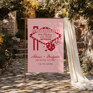 May include: Pink wedding welcome sign with a red Las Vegas sign graphic, dice, and the text "WELCOME TO A Fabulous LAS VEGAS WEDDING Adrian + Bridgette ARE GETTIN' HITCHED! 12.15.20XX"