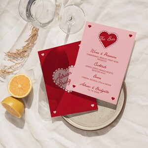 May include: Two red and pink wedding reception drink menu cards with a heart design. The top card says "The Bar" and lists wines, cocktails, and beers. The bottom card says "Adrian & Bridgette" and the date "12.15.20XX".