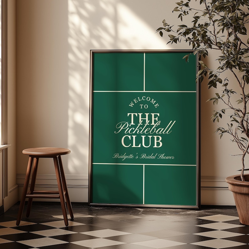 May include: A framed sign with a dark green background and white lines, resembling a pickleball court. The text reads "WELCOME TO THE Pickleball CLUB" and "Bridgette's Bridal Shower."