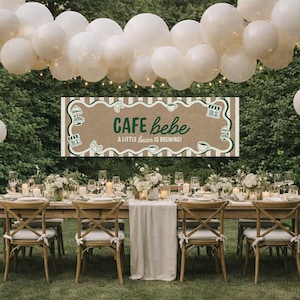 Op de afbeelding: Een buitendiner met een lange houten tafel. Witte ballonnen en bloemstukken versieren de ruimte. Een bord leest "Cafe Bebe, A Little Bean Is Brewing!"