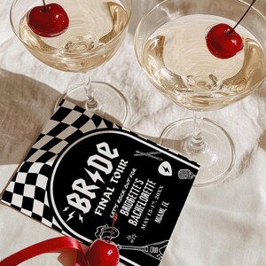 May include: Black and white checkered invitation with the text "Bride Final Tour Let's rock out for Bridgette's Bachelorette May 15-17, 20XX Miami, FL". Two champagne flutes with cherries on the rim.