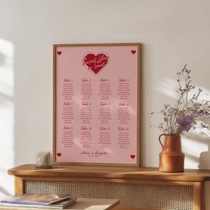 May include: A pink and red wedding seating chart with a heart design and the text "Saved You a Seat". The chart lists tables and guest names for a wedding reception.
