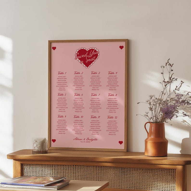 May include: A pink and red wedding seating chart with a heart design and the text "Saved You a Seat". The chart lists tables and guest names for a wedding reception.