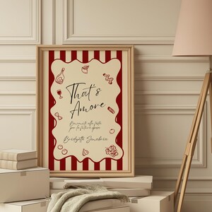 May include: A framed print with a cream-colored background and a red and white striped border. The print features the words "That's Amore" in elegant script, along with Italian text and illustrations of food and drink.