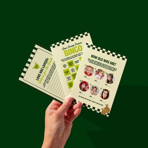 May include: Three printed cards with a green and white theme are held against a dark green background. The cards feature text and graphics, including the words "LOVE HAS LAVERS", "BINGO", and "HOW OLD WAS SHE?" The cards are designed for a bridal shower.