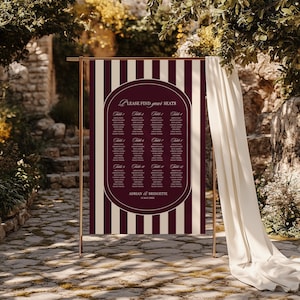 May include: A wedding seating chart with a burgundy and cream striped background. The chart features a burgundy oval with the text "Please find your seats" and guest names listed under table numbers. The names Adrian & Bridgette are at the bottom.