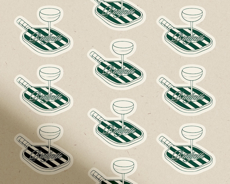 May include: A repeating pattern of stickers featuring a cocktail glass atop a green and white striped paddle. The word "Bridgelle" is written in cursive on the paddle. The background is a light beige color.