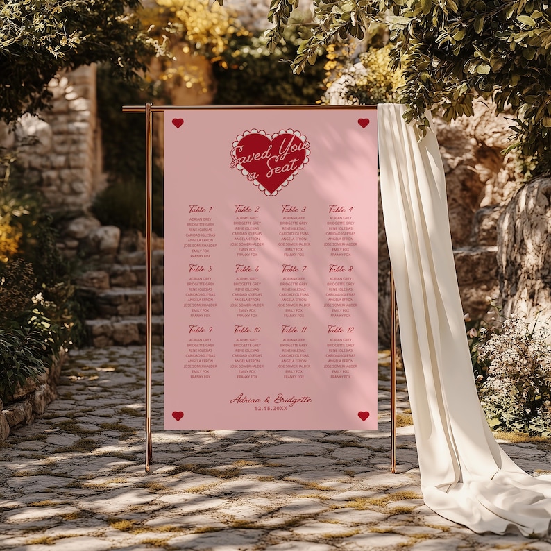 May include: Pink wedding seating chart with a red heart and the text "Saved Your Seat". The chart lists tables with guest names for a wedding reception. The bottom of the chart reads "Adrian & Bridgette 12.13.20XX".