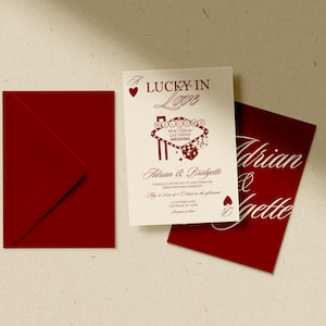 Puede incluir: Un conjunto de invitaciones de boda con un sobre rojo, una tarjeta de invitaci&oacute;n blanca con texto rojo y una tarjeta roja con escritura blanca. La invitaci&oacute;n dice "Lucky in Love" e incluye los nombres Adrian & Bridgette.