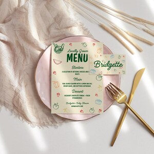 May include: A baby shower menu and place card with a pink plate, gold utensils, and decorative elements. The menu reads "Locally Grown Menu" with starter, main, and dessert options. The place card says "Bridgette".
