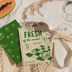 Op de afbeelding: Een cr&egrave;me- en groene bruidsdouche-uitnodiging met de tekst "FRESH off the market". De uitnodiging bevat de datum, tijd en locatie. Een groene kaart met fruitillustraties staat naast de uitnodiging. Een halve papaja en een glas water zijn ook zichtbaar.