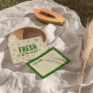 Op de afbeelding: Een stilleven met een gehalveerde papaja, een keramische kom en twee kaarten. E&eacute;n kaart toont de tekst "FRESH off the market" in het groen. De andere is een receptkaart. De sc&egrave;ne is op een witte doek.
