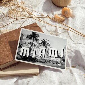 May include: Black and white postcard with a photo of palm trees and buildings in Miami, Florida. The text on the postcard reads "We're going to Miami!" and "Bridget's Bachelorette May 15-17, 20XX".