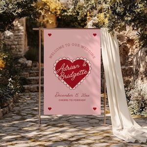 May include: Pink wedding welcome sign with a red heart and the text "Welcome to our wedding Adrian & Bridgette December 15, 20xx Cheers to forever!"