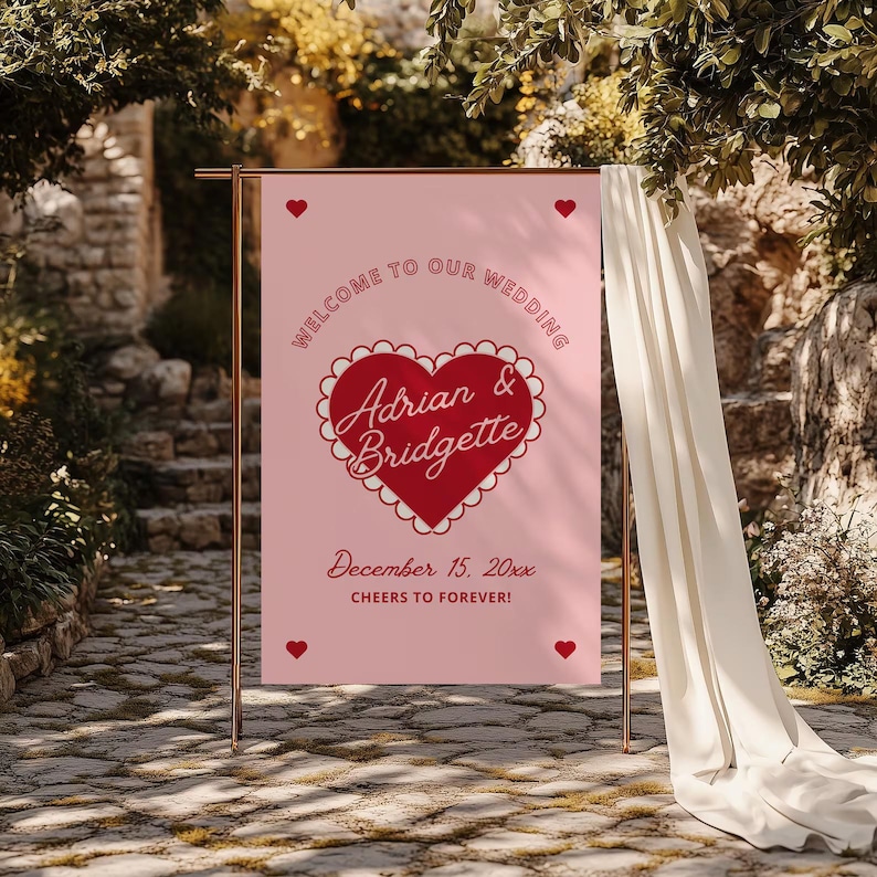 May include: Pink wedding welcome sign with a red heart and the text "Welcome to our wedding Adrian & Bridgette December 15, 20xx Cheers to forever!"