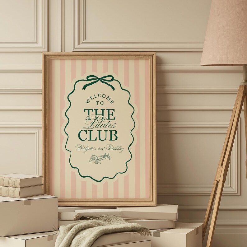 Puede incluir: Un letrero enmarcado con un fondo a rayas rosas y blancas. El letrero tiene un borde decorativo verde y el texto "WELCOME TO THE Pilates CLUB" con "Bridgette's 21st Birthday" debajo. El marco es de color marr&oacute;n claro.