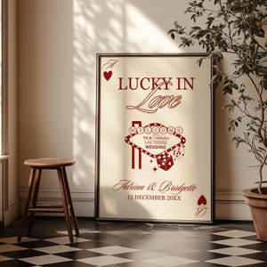 Puede incluir: P&oacute;ster enmarcado con el texto "LUCKY IN Love" en borgo&ntilde;a. Presenta un dise&ntilde;o de letrero de Las Vegas, dados, los nombres "Adrian & Bridgette" y la fecha "15 DECEMBER 20XX". El fondo es de color beige claro.