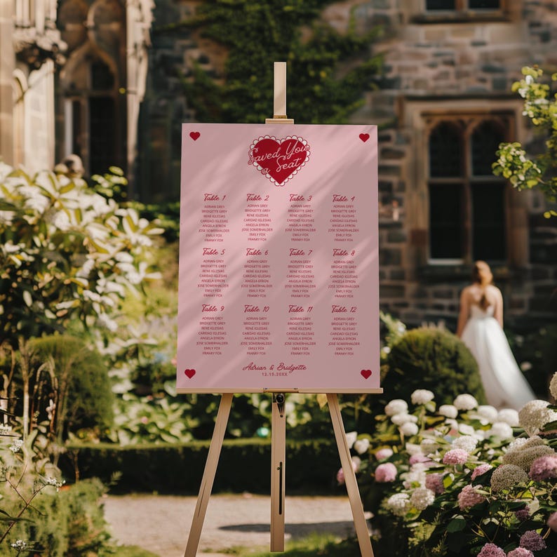 May include: Pink wedding seating chart with a red heart and the text "Saved You a Seat". The chart lists tables with guest names and the date "12.18.2022".