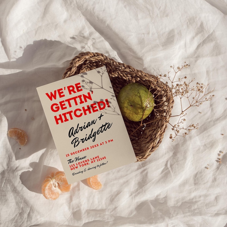 May include: A tan wedding invitation with red text that reads "We're Gettin' Hitched!"  Adrian + Bridgette. The invitation includes the date, time, and location of the wedding.