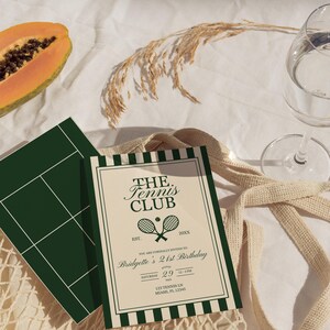 May include: A tennis-themed invitation with the text "The Tennis Club" and a tennis court graphic. The invitation is cream-colored with dark green accents and includes event details. A slice of papaya and a glass of water are also present.