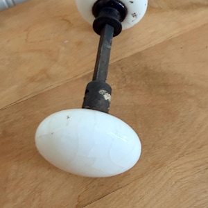May include: Antique white porcelain door knob set with a black metal stem. The knobs are oval-shaped and show a crackle pattern. The door knob set is a vintage item.