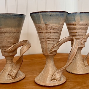 May include: Three ceramic cups with a light blue glaze and a brown and white striped pattern. Each cup has a unique handle that resembles a leaf or a branch.