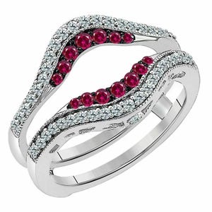 Könnte beinhalten: Ein silberner Ringschutz mit geschwungenem Design. Der Ringschutz ist mit kleinen, runden, roten Edelsteinen und klaren, funkelnden weißen Edelsteinen besetzt. Die Edelsteine sind in einem wellenförmigen Muster angeordnet und erzeugen einen eleganten Look.