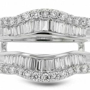 May include: A white gold ring guard with a double-band design. The bands are adorned with numerous round and baguette-cut diamonds, creating a sparkling, elegant appearance. The ring guard is designed to enhance the look of a solitaire ring.
