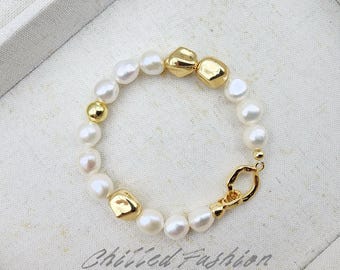 May include: A white pearl bracelet with gold-colored accents. The bracelet features a mix of round and irregularly shaped pearls, interspersed with gold-colored beads and larger, textured gold-colored elements. A gold-colored clasp secures the bracelet.