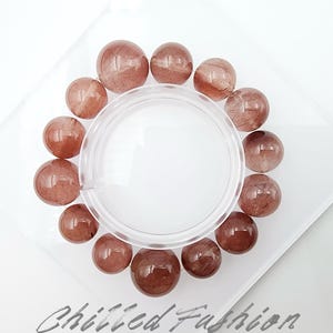 May include: A clear glass container surrounded by a circle of reddish-brown gemstone beads. The beads are arranged on a clear, square surface. The words "Chilled Fashion" are written in cursive at the bottom.