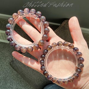 May include: Two bracelets with translucent, round, purple-brown beads. The bracelets are held in place by clear, circular holders. The bracelets are on a light skin tone background. The text "Chilled Fashion" is in the upper right corner.