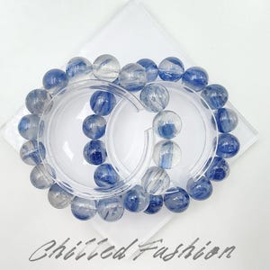 May include: A pair of bracelets with translucent blue and white beads. The beads are arranged in a circular pattern, resting on a white surface. The text "Chilled Fashion" is visible at the bottom of the image.