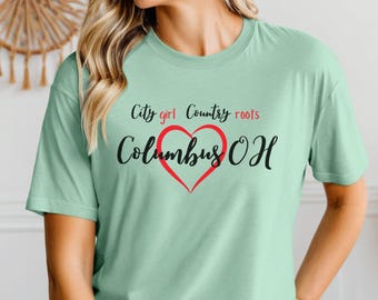 Może przedstawiać: Jasnozielona koszulka z napisem "City girl Country roots Columbus OH" w kolorze czarnym i czerwonym. Słowo "Columbus" jest napisane kursywą, z czerwonym sercem. Koszulka ma krótkie rękawy.
