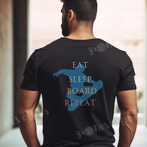 Può includere: T-shirt nera con grafica di snowboarder blu e le parole "EAT SLEEP BOARD REPEAT" in bianco e oro. Il design è sul retro, perfetto per gli appassionati di snowboard.