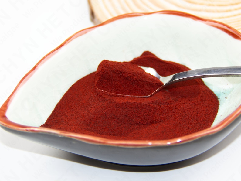 Puede incluir: Un peque&ntilde;o taz&oacute;n blanco con un borde oscuro contiene un mont&oacute;n de polvo rojo oscuro. Una cuchara de plata est&aacute; parcialmente sumergida en el polvo.