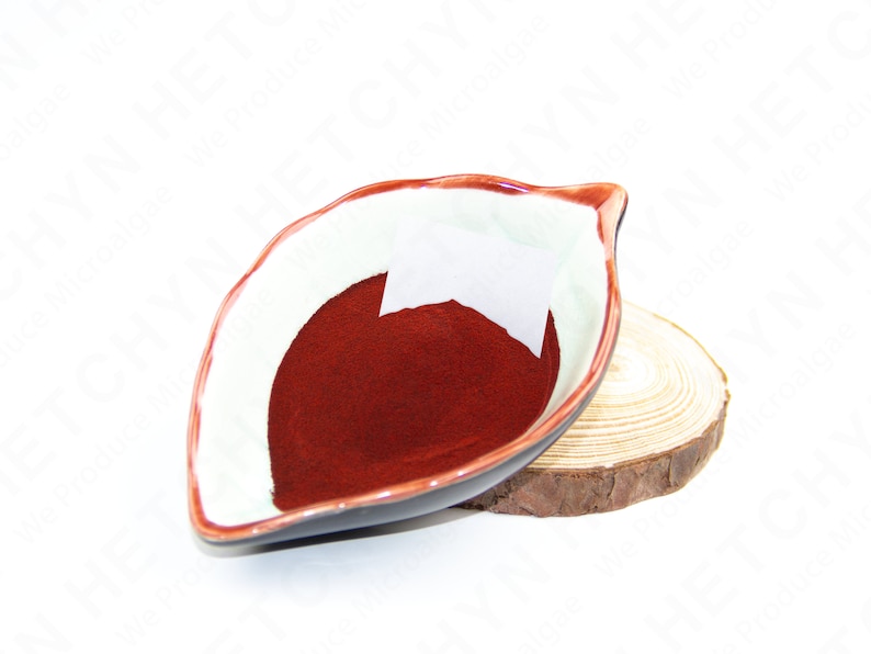 Puede incluir: Un peque&ntilde;o cuenco de cer&aacute;mica blanca con un borde rojo, con forma de hoja, lleno de un polvo rojo oscuro. El cuenco est&aacute; sobre una base de madera.