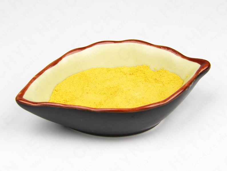 May include: A leaf-shaped ceramic bowl with a black exterior, cream-colored interior, and a reddish-brown rim. The bowl is filled with a bright yellow powder, likely a spice or ingredient.