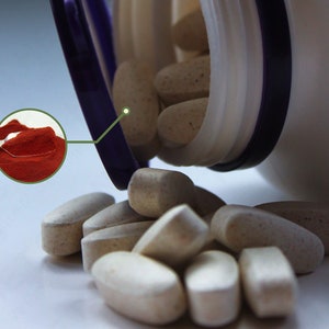 Puede incluir: Una botella de pl&aacute;stico blanca con una tapa morada est&aacute; abierta y derrama p&iacute;ldoras ovaladas de color beige. Se puede ver una peque&ntilde;a cuchara de polvo rojo en el fondo.