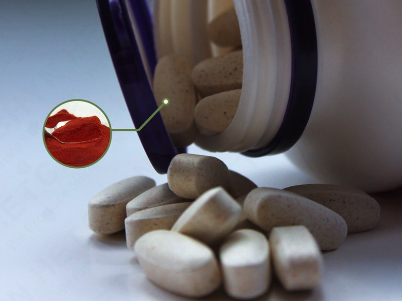 Puede incluir: Una botella de pl&aacute;stico blanca con una tapa morada est&aacute; abierta y derrama p&iacute;ldoras ovaladas de color beige. Se puede ver una peque&ntilde;a cuchara de polvo rojo en el fondo.