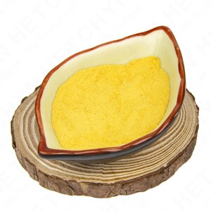 May include: A leaf-shaped ceramic bowl filled with yellow powder, resting on a round wooden slice. The bowl has a cream-colored interior with a brown rim. The wooden slice displays a natural wood grain.