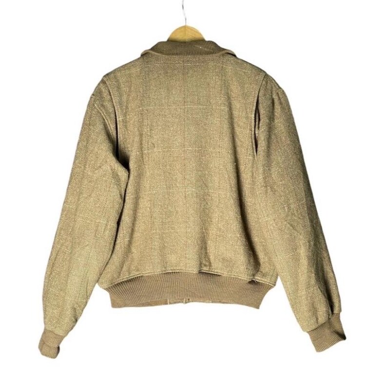 May include: Tan bomber jacket with a ribbed collar, cuffs, and hem. The jacket has a full zipper closure and a textured fabric. The jacket is hanging on a wooden hanger against a white background.